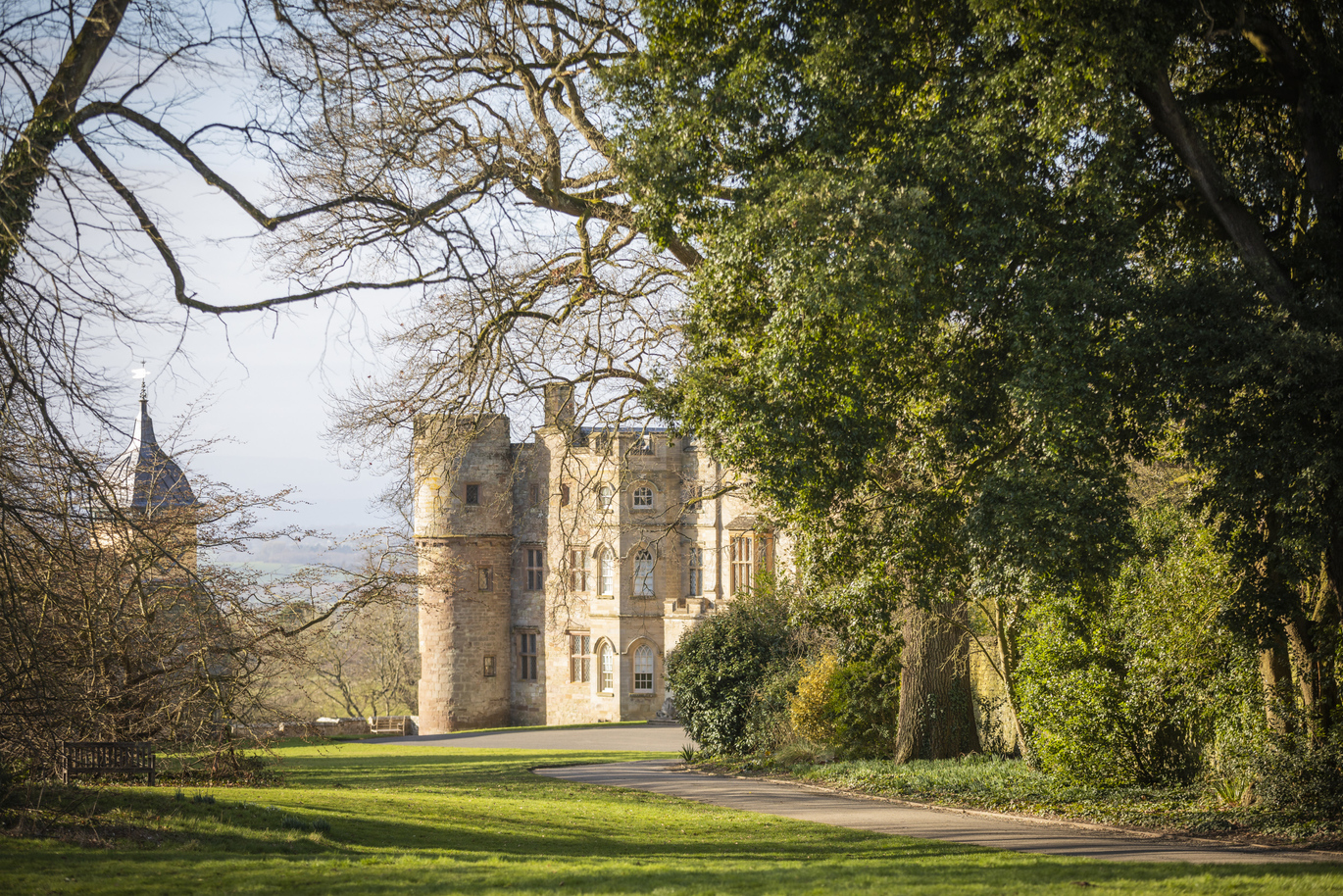 The exterior of the castellated 17th-century manor house at Croft Castle and Parkland with a path leading up to it bordered by trees and a lush green lawn.