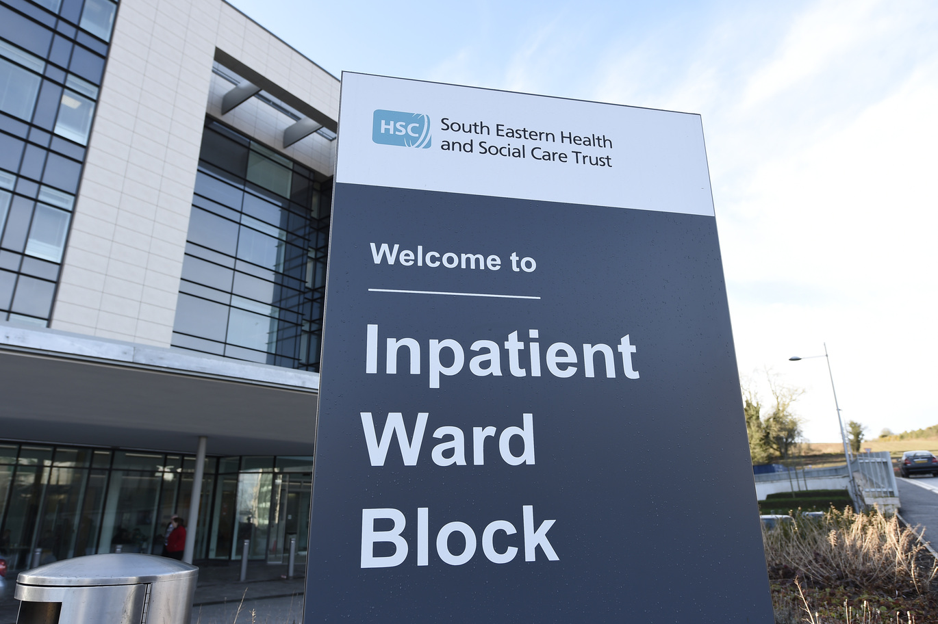 "A close up image of a sign which reads 'South Eastern Health and Social Care Trust. Welcome to Inpatient Ward Block'. In the background is Ulster Hospital."