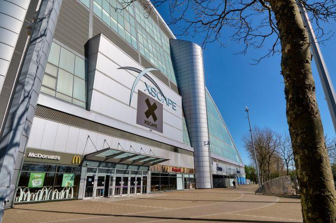 "Exterior of Xscape Milton Keynes with glass façade, large Xscape sign above entrance, and shops at ground level."