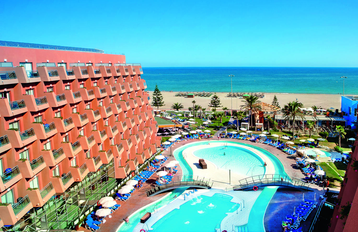 Aerial view of the hotel complex with the pool in the middle and the beach and sea behind.
