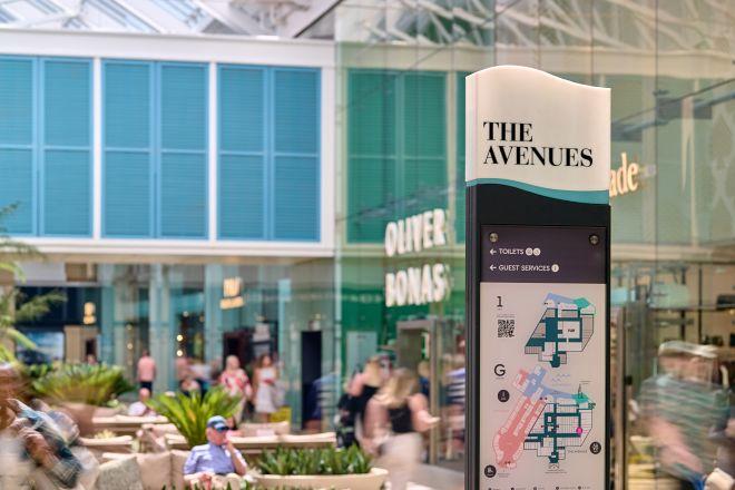 "Shopping centre information sign at The Avenues with directory map, surrounded by shops and seating"