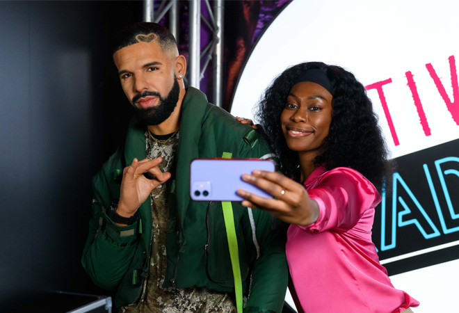 "A person taking a selfie with a wax figure of Drake"