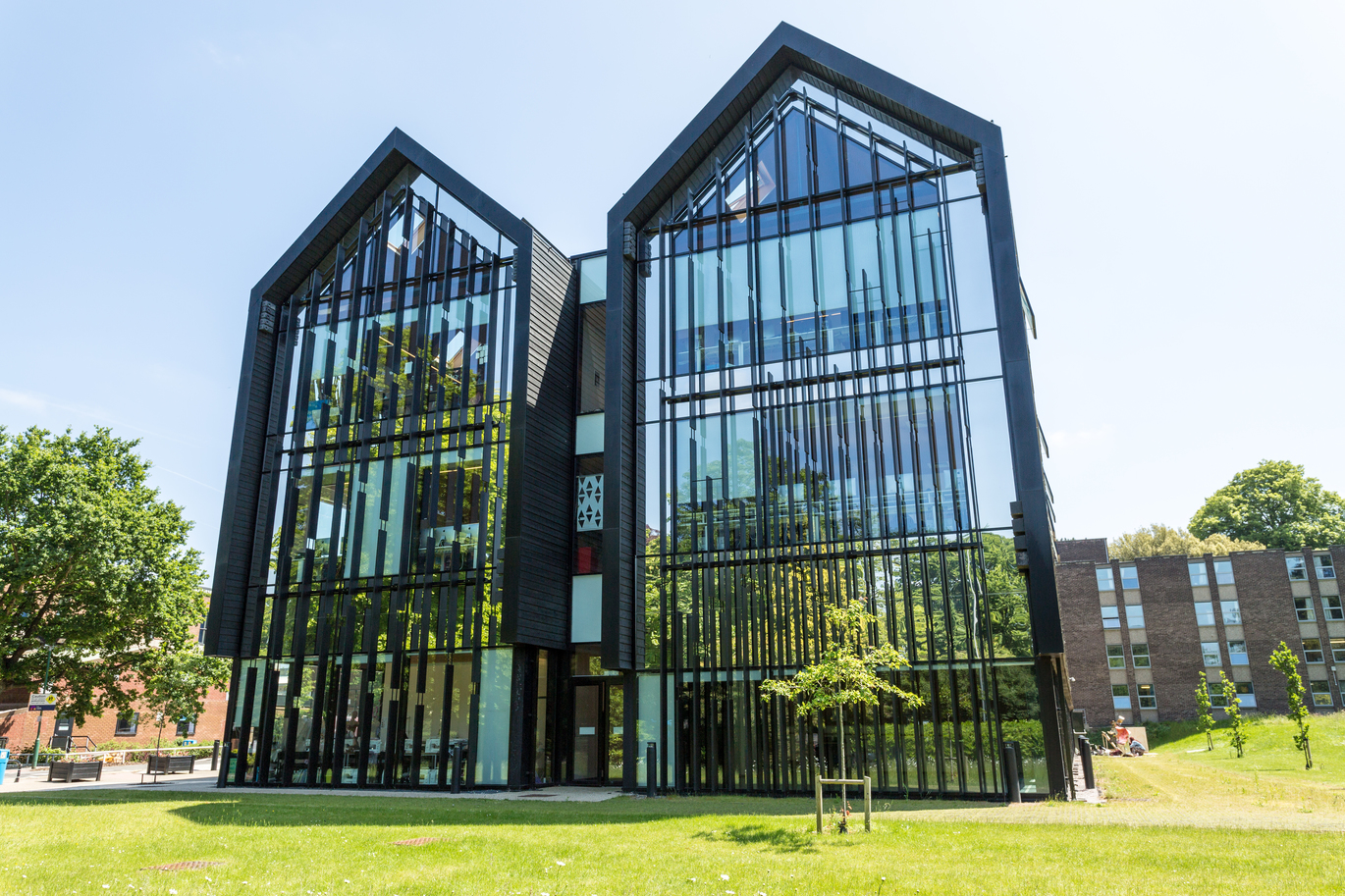 "Outside of City College Norwich building with glass facade, grass all around and blue skies"