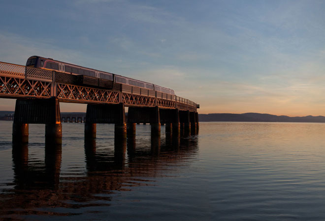"Dundee train line going over body of water with sun setting in background"