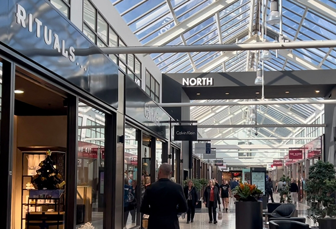 "Interior image of shopping centre with central walkway featuring shops on either side with signs and glass roof"