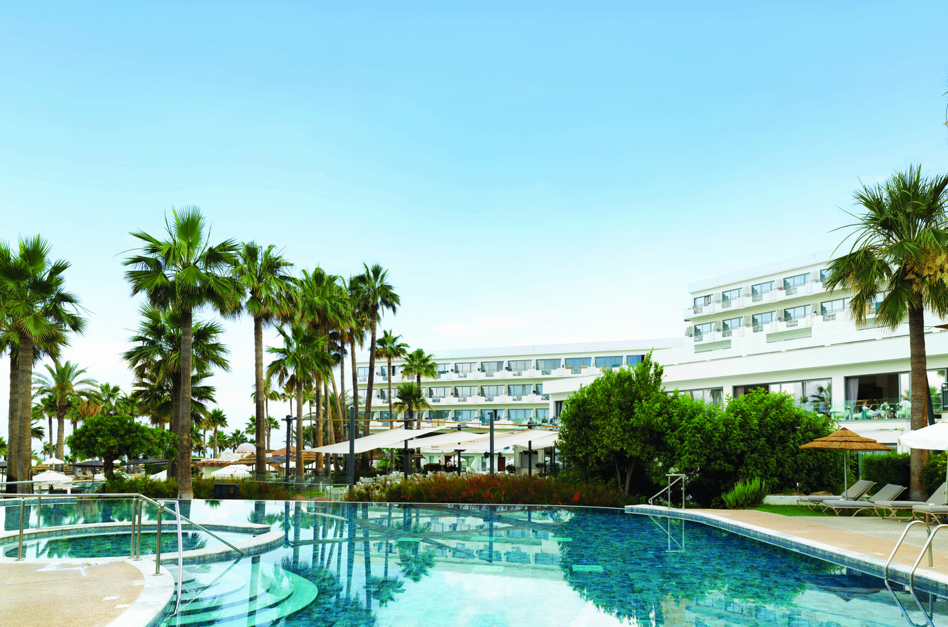 View of the pool area with palm trees behind and the hotel buildings visible behind.