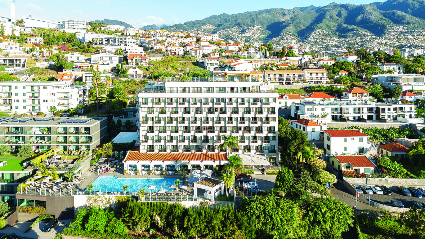 View of the hotel and pool with many other buildings around and a mountain in the background.