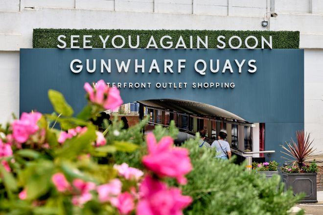 "Gunwharf Quays entrance sign with “See you again soon” message, framed by pink flowers."