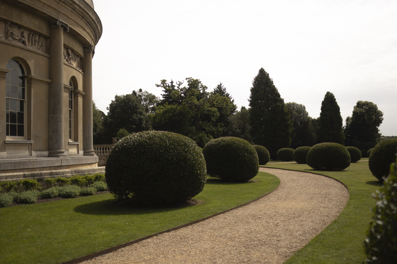 Curved gravel path and neatly clipped topiary in the Italianate Garden at Ickworth with a round sandy coloured building to the left.