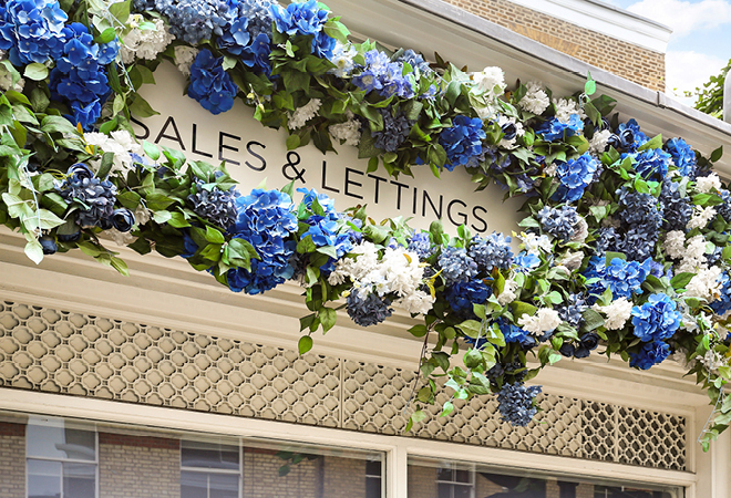 A Sales and Letting sign above a shop, surrounded by blue flowers