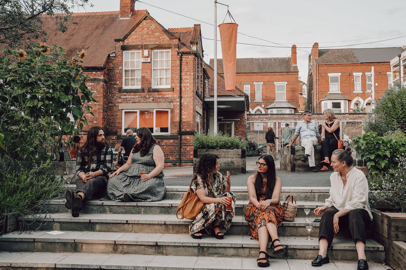 View of brick buildings outside from the bottom of concrete steps with people sitting and talking on the steps.