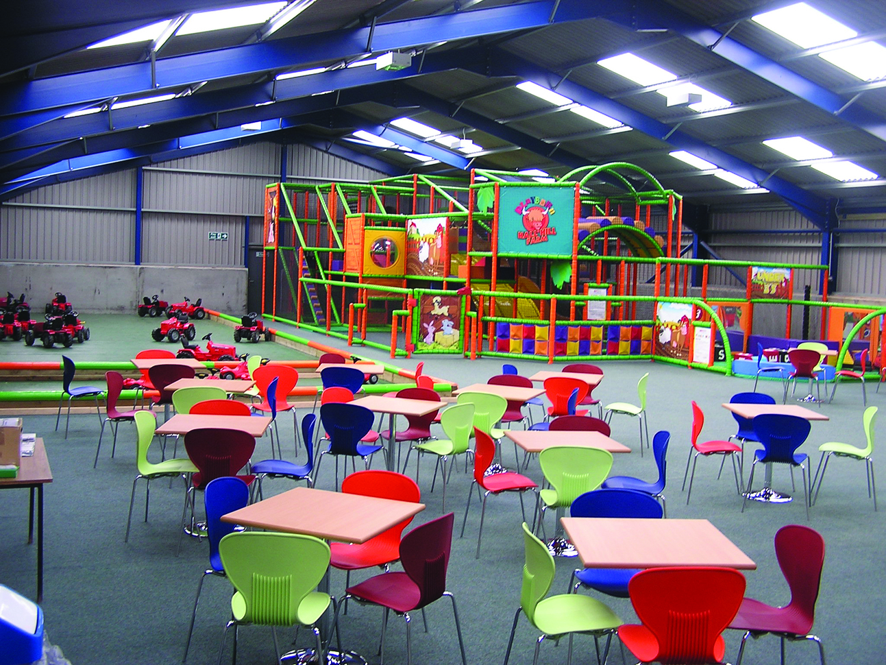 "Indoor playbarn with tables and chairs, a soft play climbing frame and push along tractors for children"