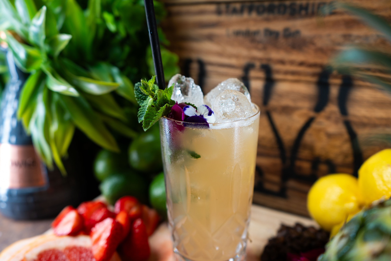 ''a cocktail drink on a table with plants and fruit in the background''