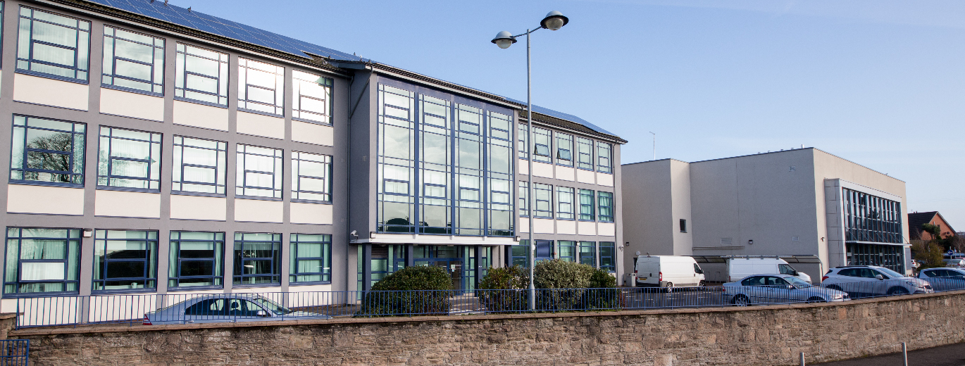 "College building with short wall and carpark in foreground"