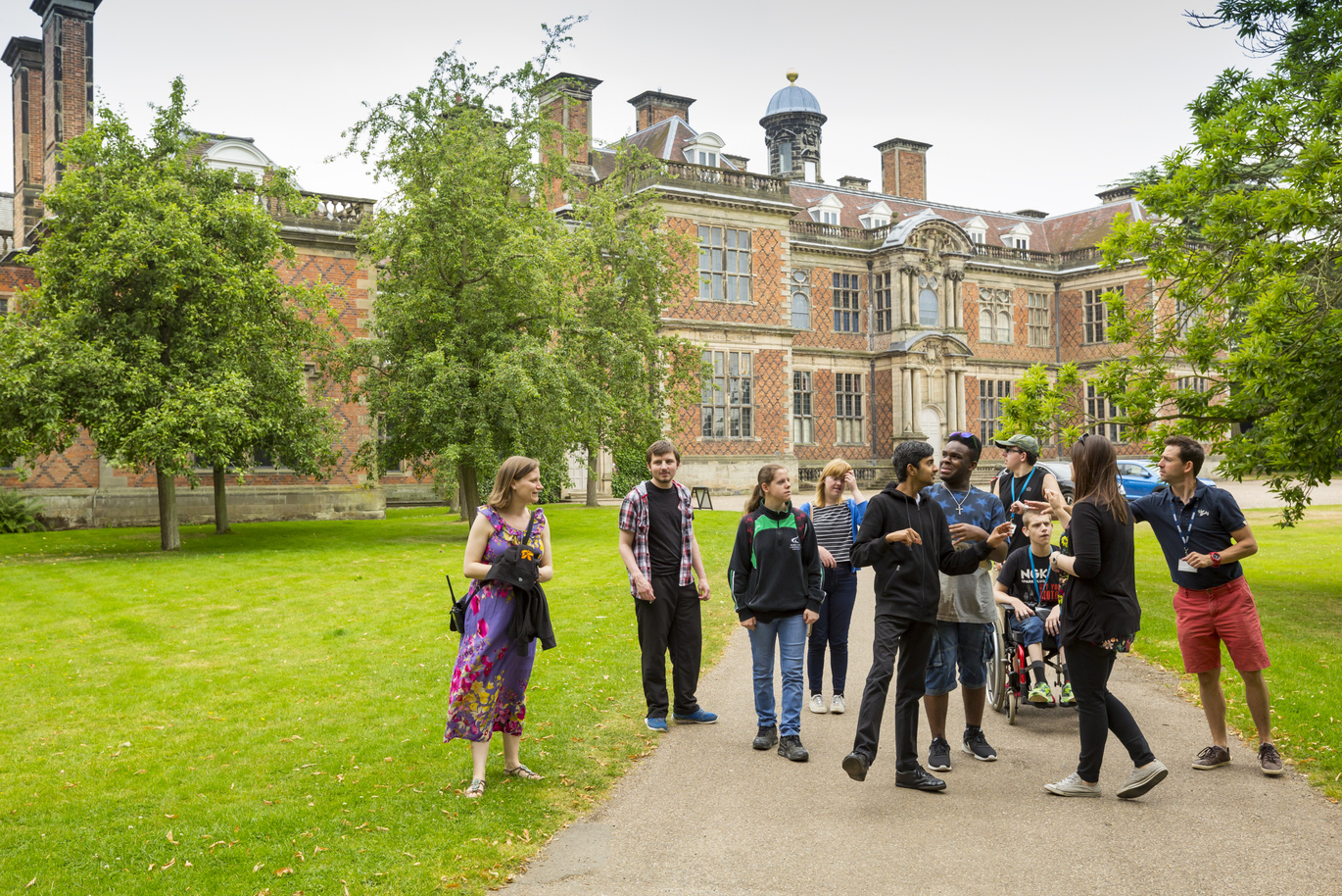 Sudbury Hall with people on the path in front. There are a number of trees around and the path has lawn either side.