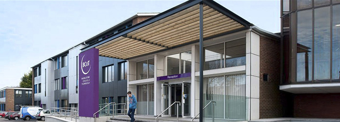 "Basingstoke College of Technology building entrance. There are steps in the middle, a ramp to the left with handrails. A person is walking down the steps away from the entrance doors."