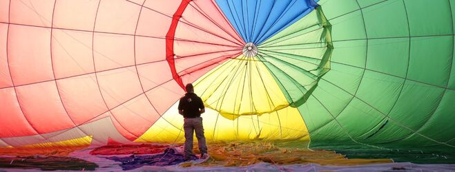 "Male standing in front of a multicolored hot air balloon"