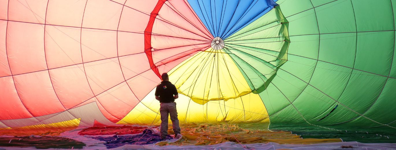 "Male standing in front of a multicolored hot air balloon"