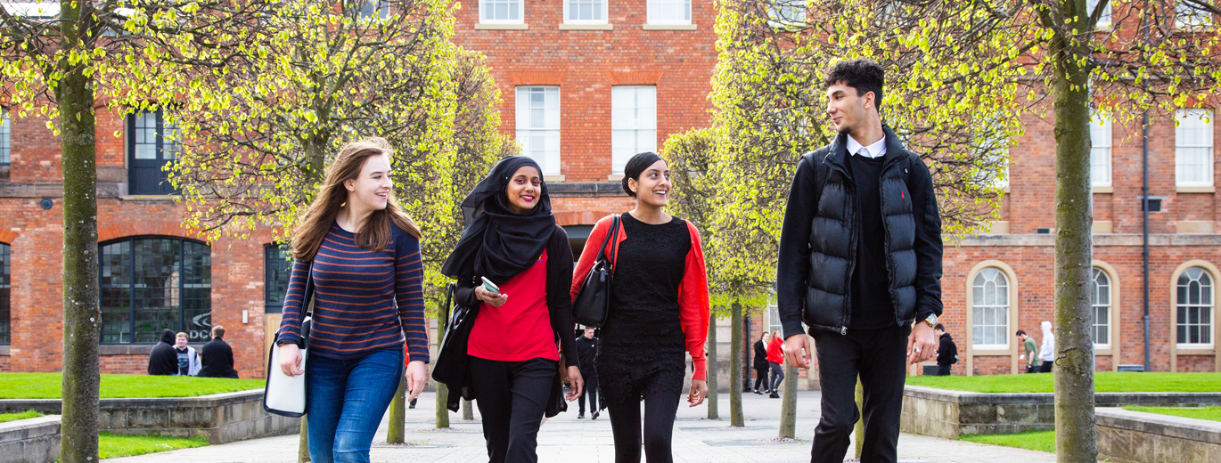 "Derby College building with four students walking and interacting in foreground"