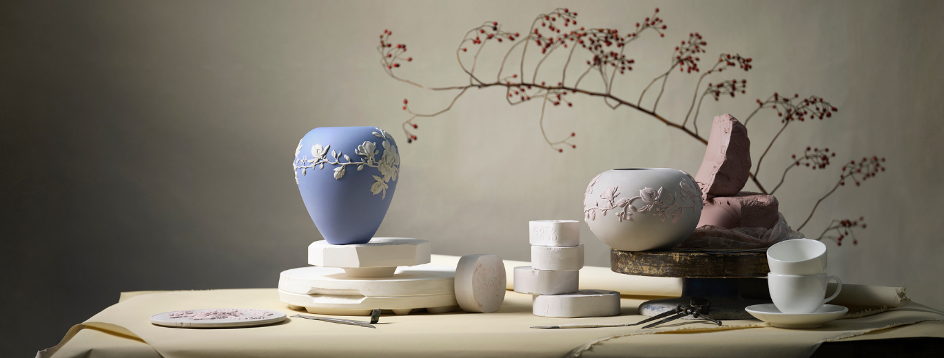 ''a blue vase on a table with a tree branch behind''