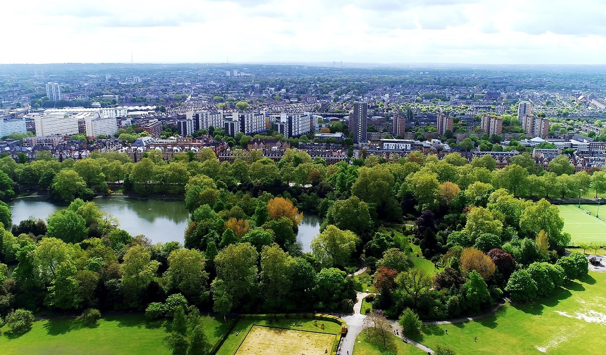 Aerial view of green space within the borough, trees and a lake in the foreground with buildings in the background.