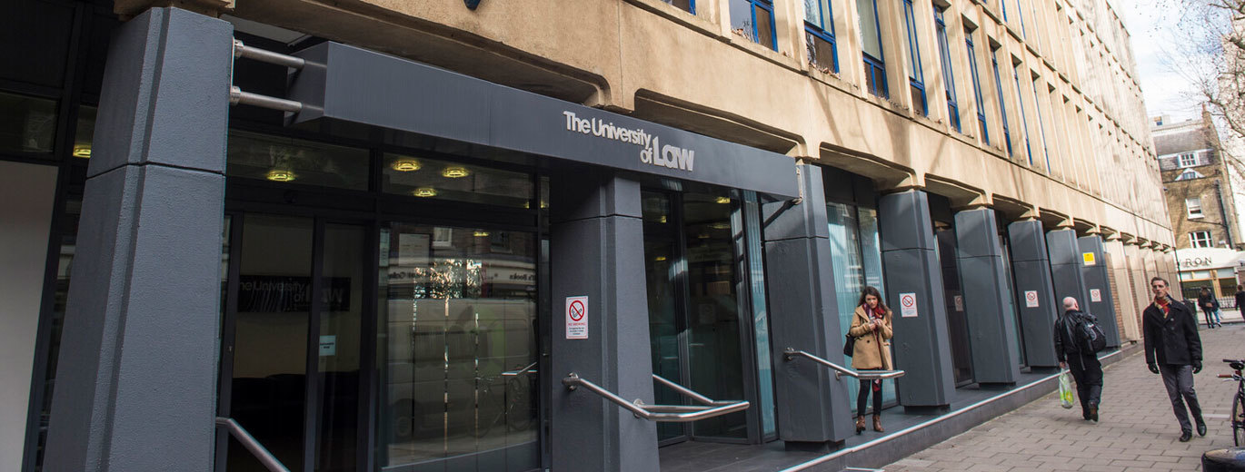 "View of The University of Law entrance to the bloomsbury campus. A pedestrian walkway is in view, with several people walking past the entrance."