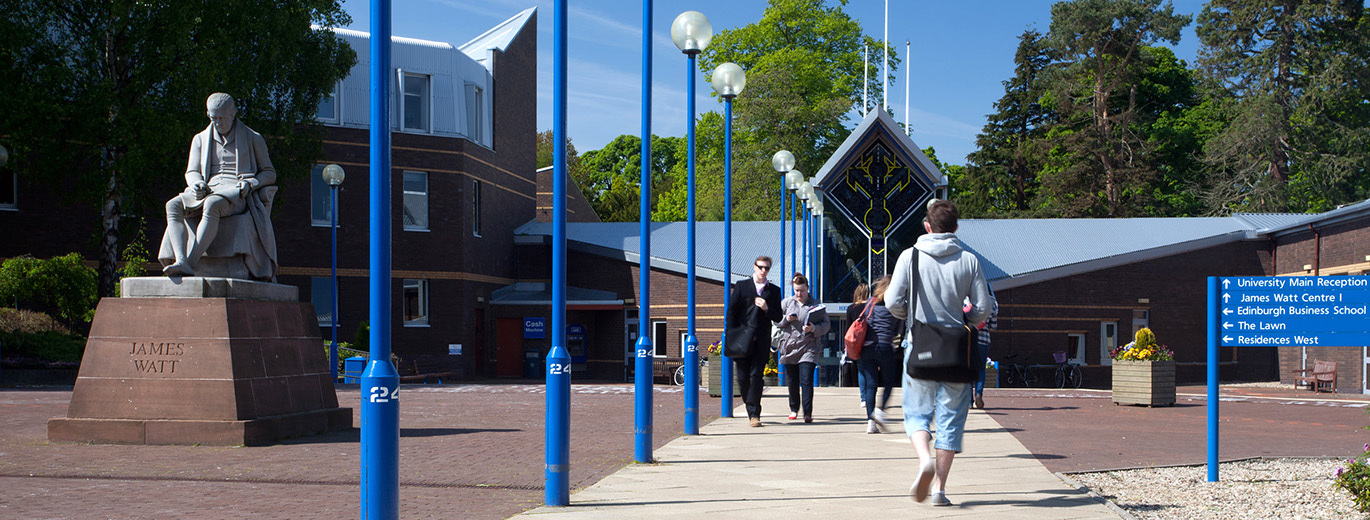 "Statue of man reading on left with walkway and students walking towards university building"