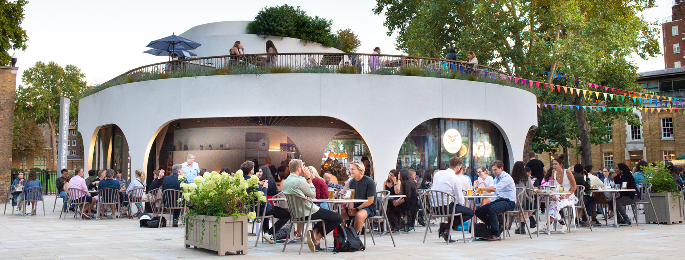Photo of people sitting at tables and chairs outside in Duke of York Square outside a restaurant. There is rainbow coloured bunting going from the restaurant roof across to other buildings.