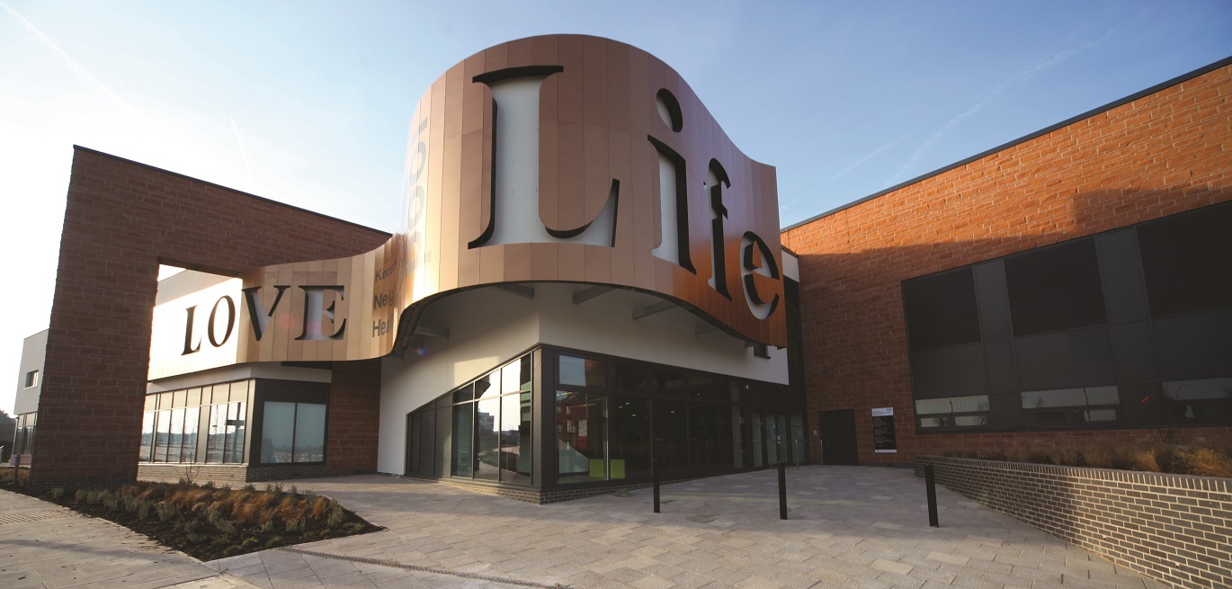 Photo of Kensington Neighbourhood Centre in Liverpool. The main entrance has a large wooden sign about with 'Love Life' going across the top of the building