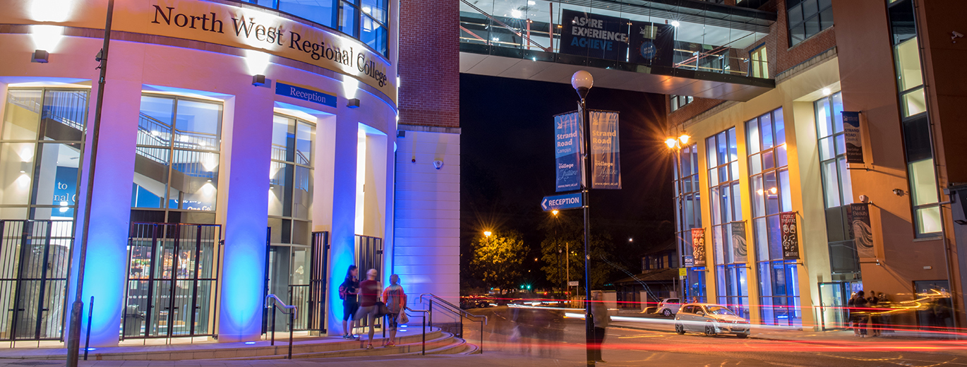 "North West Regional College entrance at night with overhead walkway."