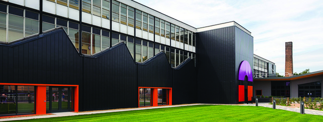 "Outside of City College Norwich building with green grass in front and blue skies behind "
