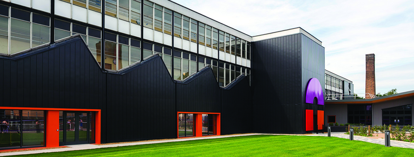 "Outside of City College Norwich building with green grass in front and blue skies behind "