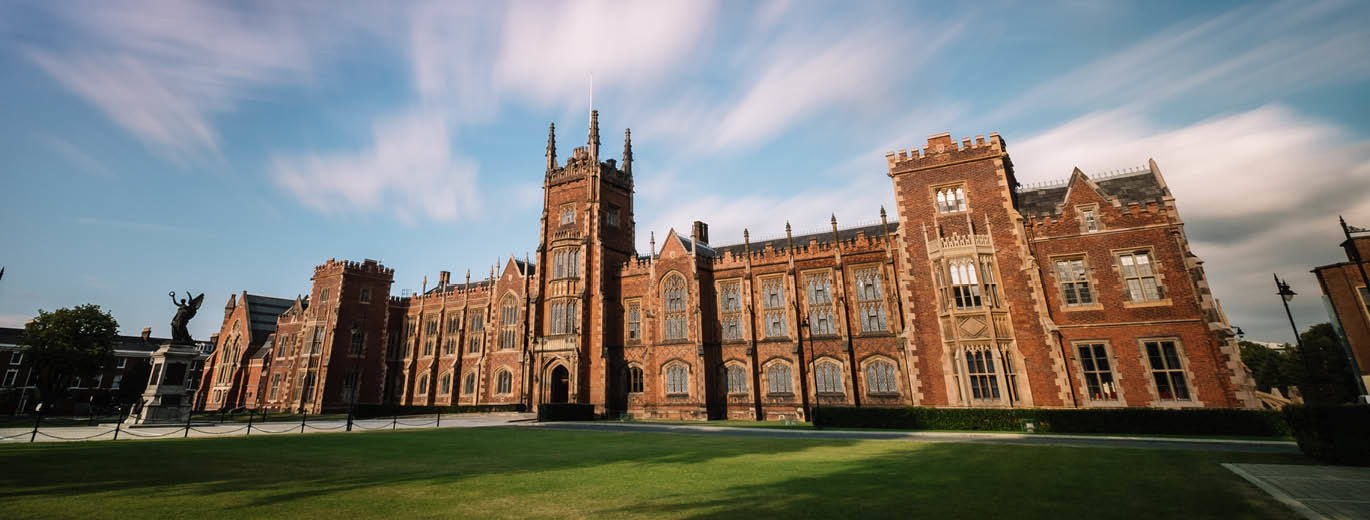 "Queen's University Belfast building with green lawn in foreground and cloudy blue skies above"