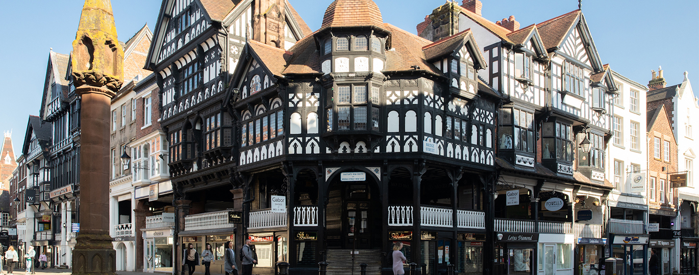 "Chester Cross, a black and white Tudor style building on the corner of a street, joining up with Bridge Street in Chester City Centre"