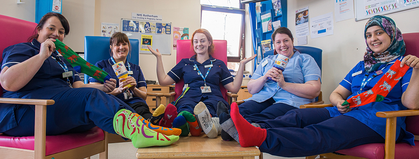 "Rotherham NHS staff seated holding charity fundraiser pots and wearing multicoloured socks for a charity day"