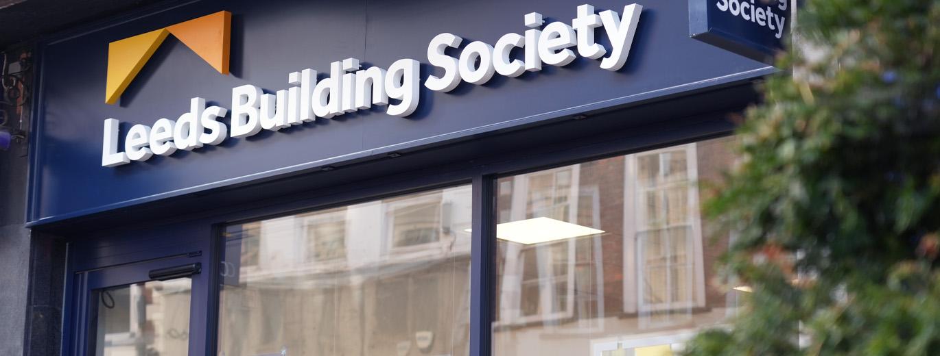 "Exterior of a Leeds Building Society branch showing the blue storefront fascia with large white Leeds Building Society signage and logo above the entrance windows."