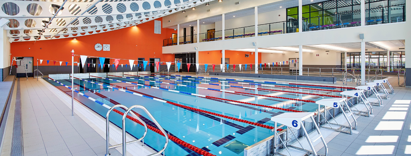 ''swimming pool with seating area above, the pool has red, white and blue lane divides and flags''