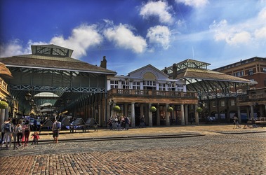 Photo of entrance to Covent Garden Market Building. There are stands throughout the market building to the left. The building to the right has pillars in front of the access to the building.