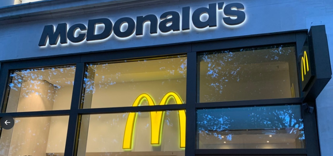 "Photo of a McDonald's entrance taken from outside. There is a large 'M' symbol located at the top of the wall inside and a McDonald's sign above the entrance outside."ght and is open."