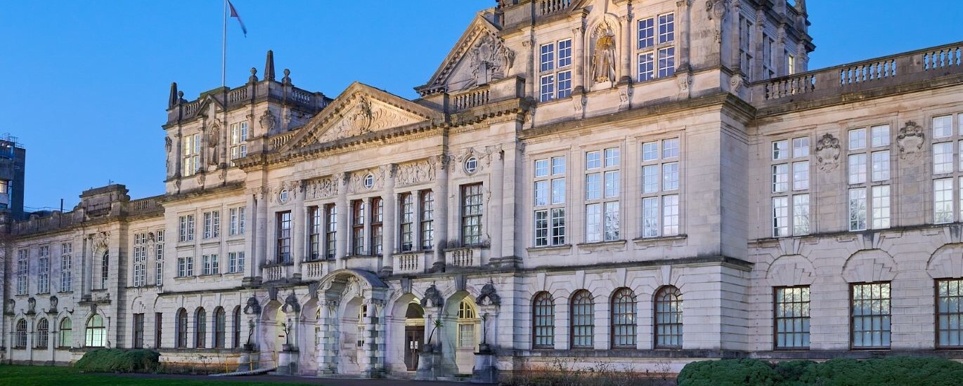 "External of Main Building at Cardiff University, large white building over three floors. Grassy area to the front"