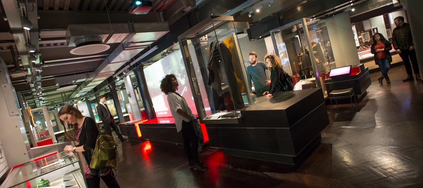 "Photo inside showing various exhibit information and displays, there are people looking at displays in the room."