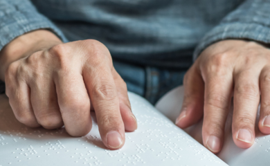 A pair of male hands reading the pages of an open book written in Braille.