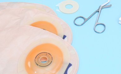 Stoma supplies laid out on a pale blue table, including ostomy bags and medical scissors.