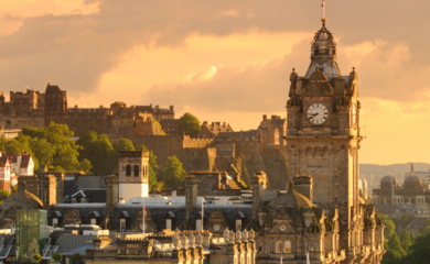 Edinburgh at sunset, showing historic buildings and clock tower with the famous castle on the hill in the distance.