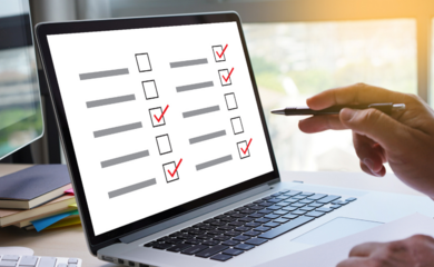 A hand holding a pen pointing to the screen of a laptop, which shows a questionnaire with boxes to tick.