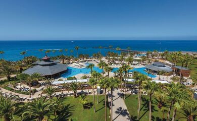 Ligging Rui Palace resort in Tenerife, showing an overview of a beautiful hotel with curving blue pools and palm trees, overlooking the sea.