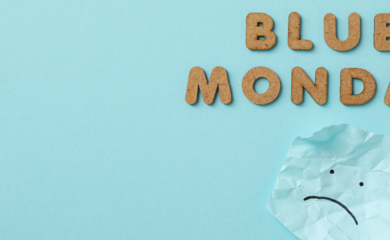 The image has a light blue background. The words Blue Monday appear in the top right hand corner in a light brown colour. There is a crumpled piece of paper underneath the text, which has a simple sad face drawn on it in black pen.
