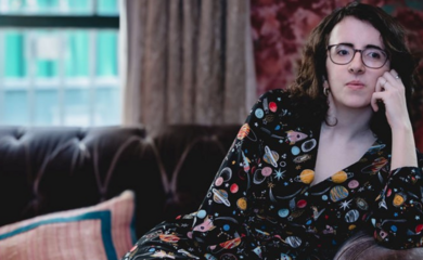 A white, disabled woman curls up on the sofa of a 1920s bar