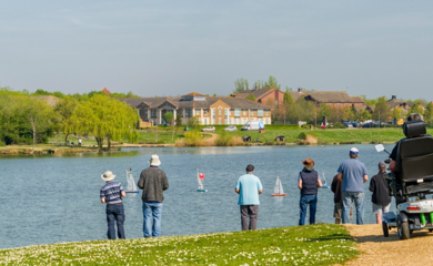 Photo of Furzton Lake with a group of people standing and one person in a wheelchair operating remote control boats.