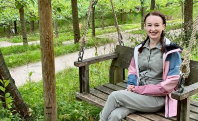 Photo of Pippa Stacey, a white woman with hair in pigtails, on a swinging bench in a forest.